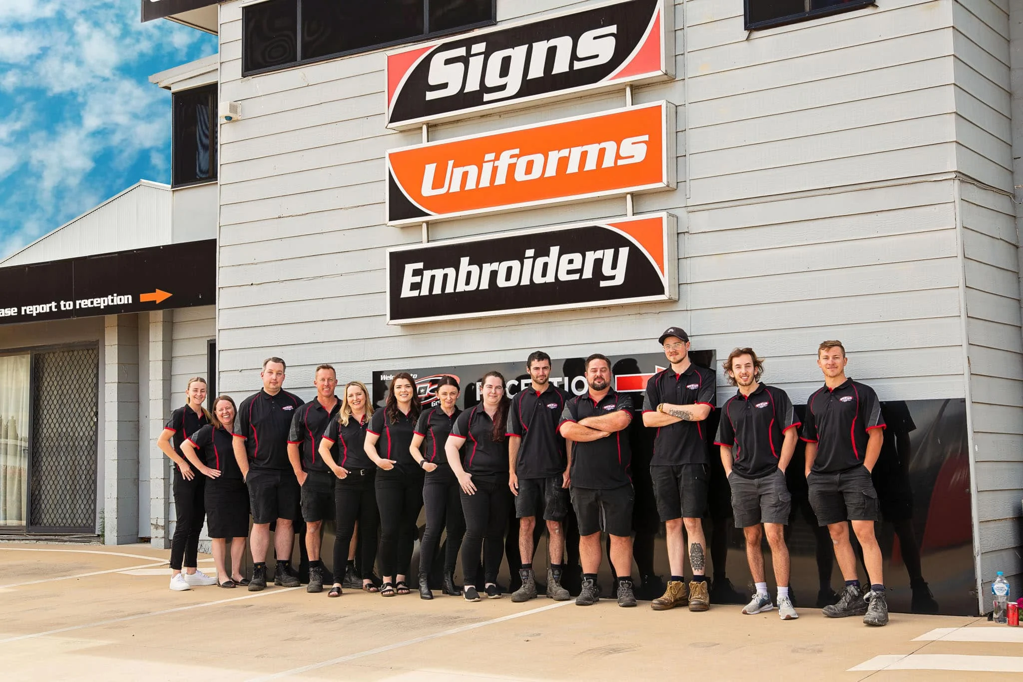 The ALE team standing in front of the Signs, Uniforms and Embroidery building