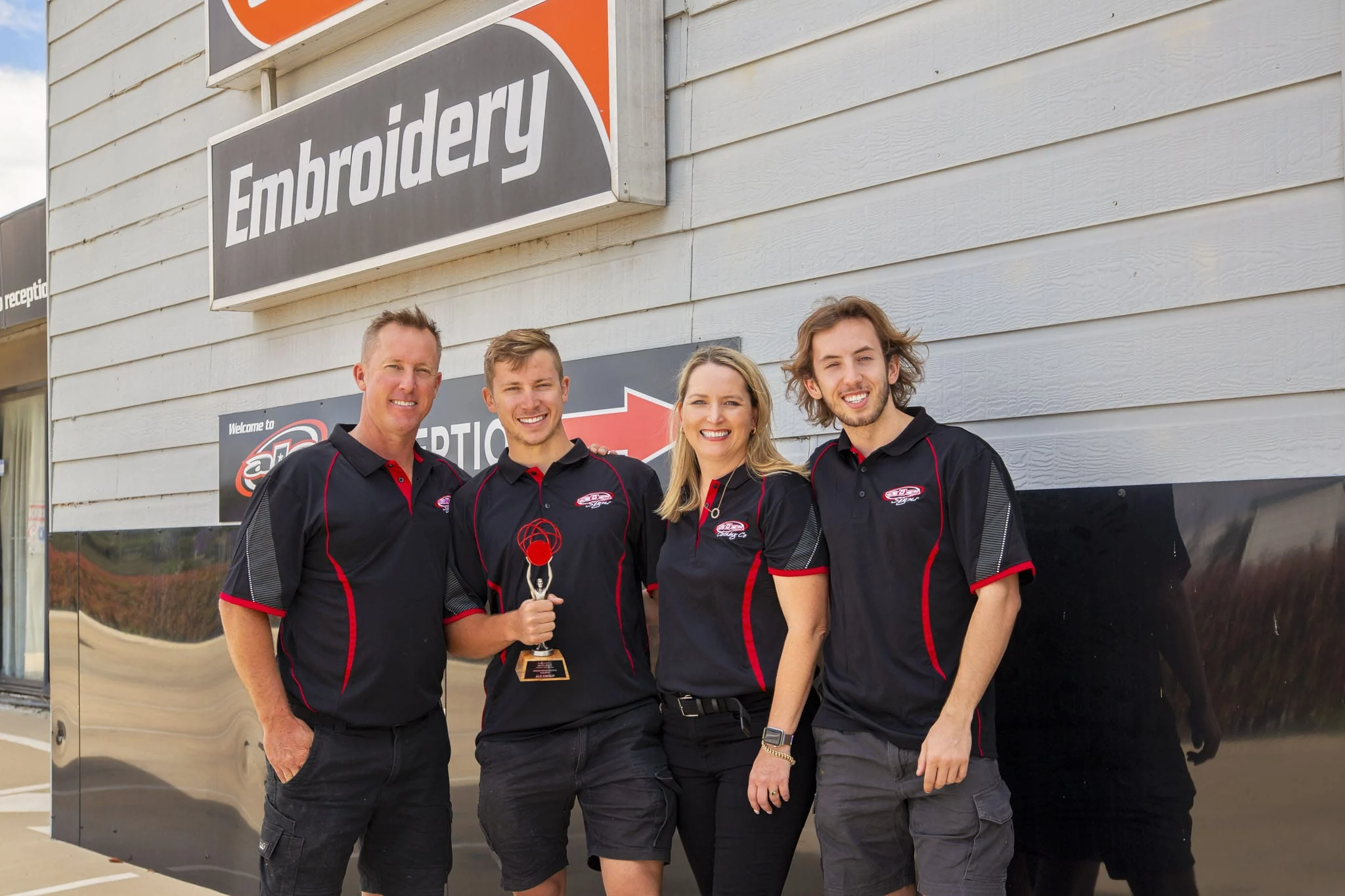 Four ALE team members holding the 2022 Business Excellence award outside the Embroidery building